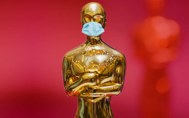 Mavi cerrahi maske takmış altın Oscar heykelciği, kırmızı fonda